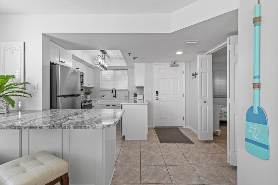 Step into this inviting kitchen with sleek granite countertops, stainless steel appliances, and a cozy breakfast bar. The coastal decor adds a welcoming beach vibe to this bright, open space.