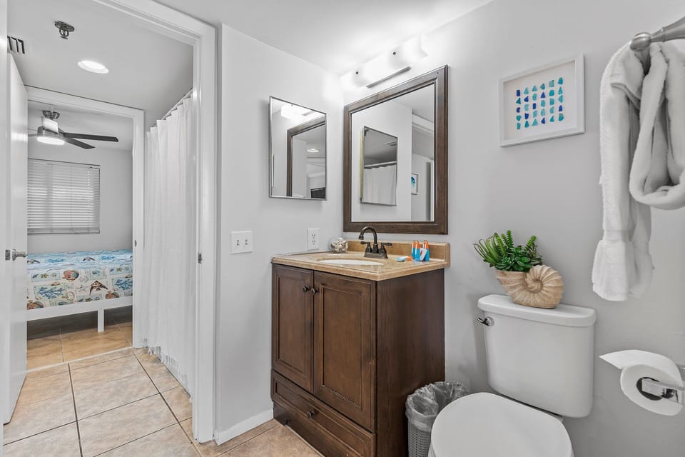 This clean bathroom features a dark wood vanity, granite countertop, and bright lighting. The space includes a shower, fresh towels, and charming coastal decor, providing a comfortable and functional environment for guests.