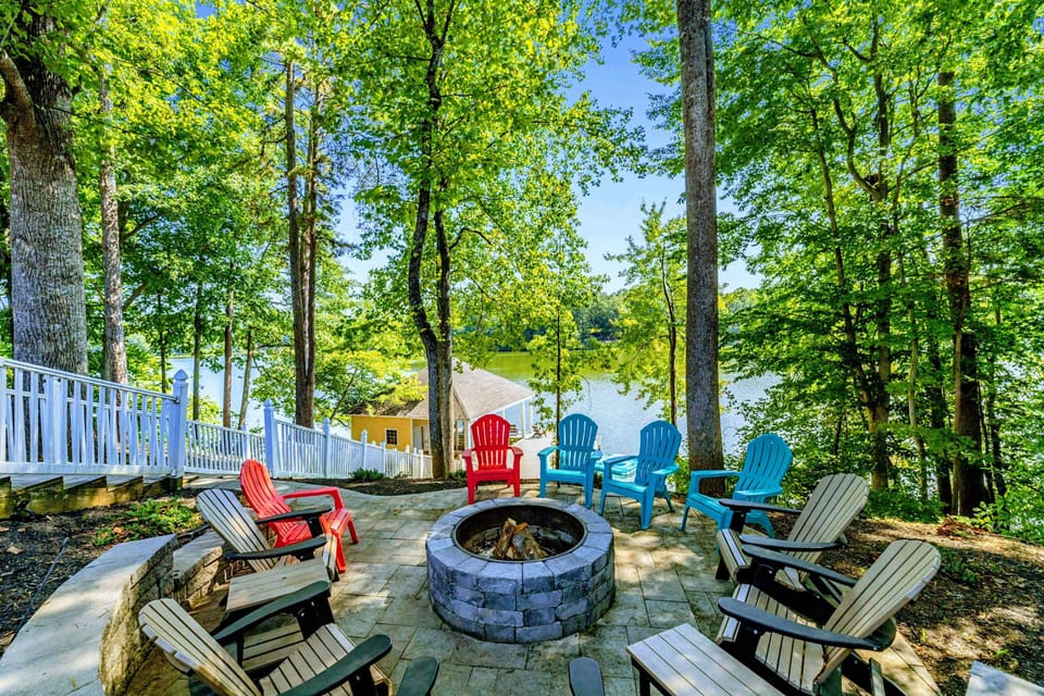 Fire Pit - Colorful Adirondack chairs circle the stone fire pit, with the lake shimmering through the trees.