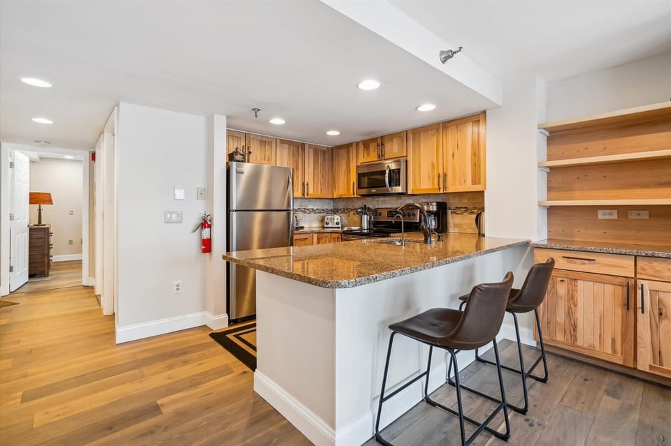 This renovated kitchen features warm wood cabinetry, granite countertops, and seating for casual dining.