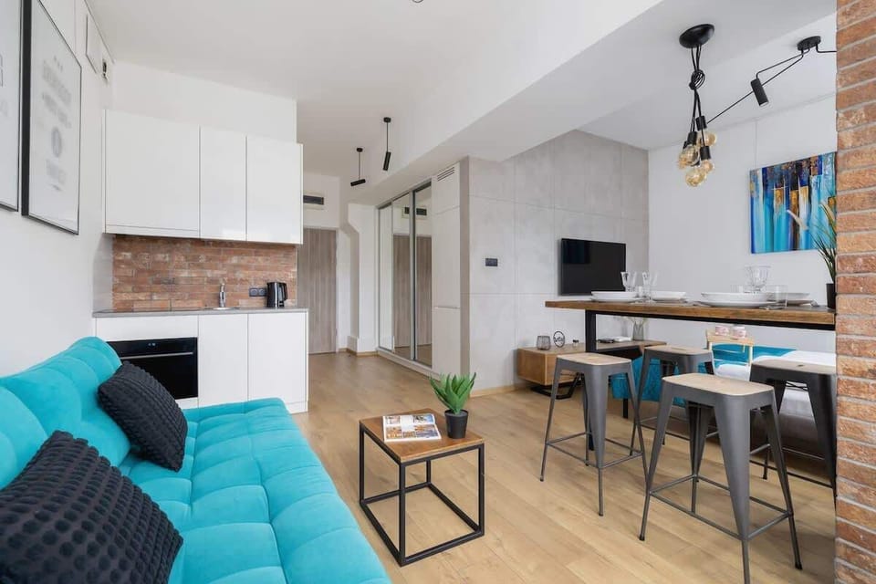 A spacious and open-plan apartment with a well-lit living area, turquoise accents, and a functional kitchen, ensuring both comfort and style.

