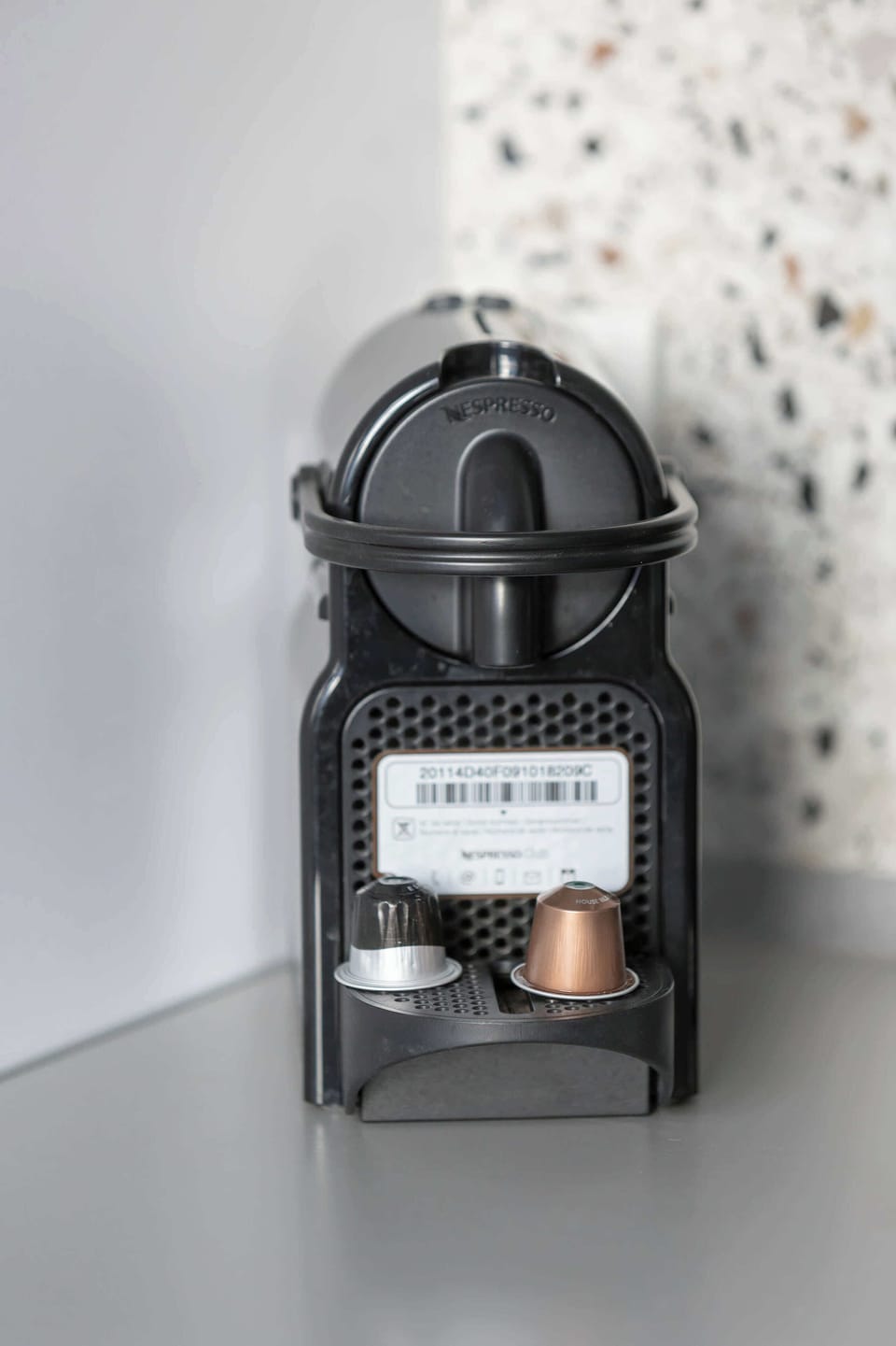 A close-up of a compact coffee machine, placed against a textured backsplash for a modern touch.






