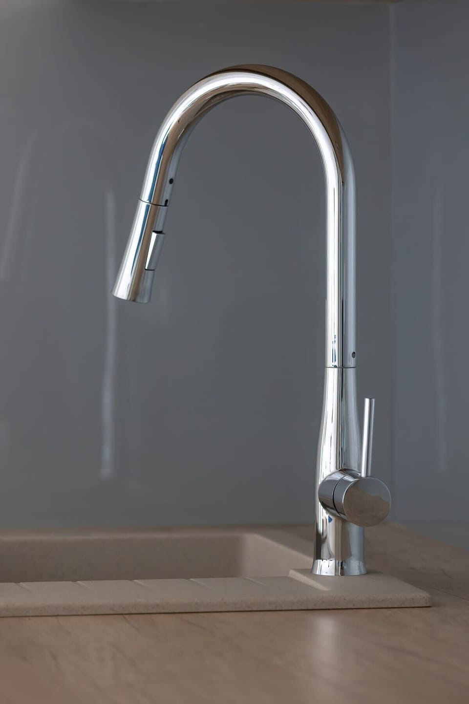 A close-up of a modern chrome kitchen faucet, standing out against the dark gray background.

