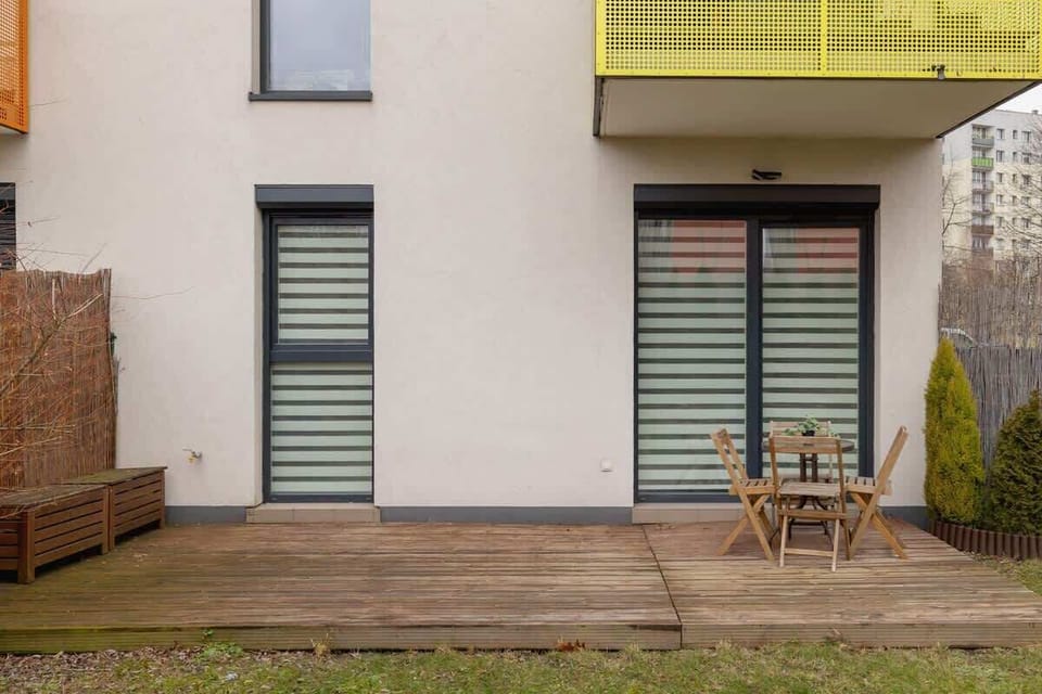 An exterior view of the apartment, featuring a private garden area with a small patio, large windows, and a balcony above, adding charm to the outdoor space.

