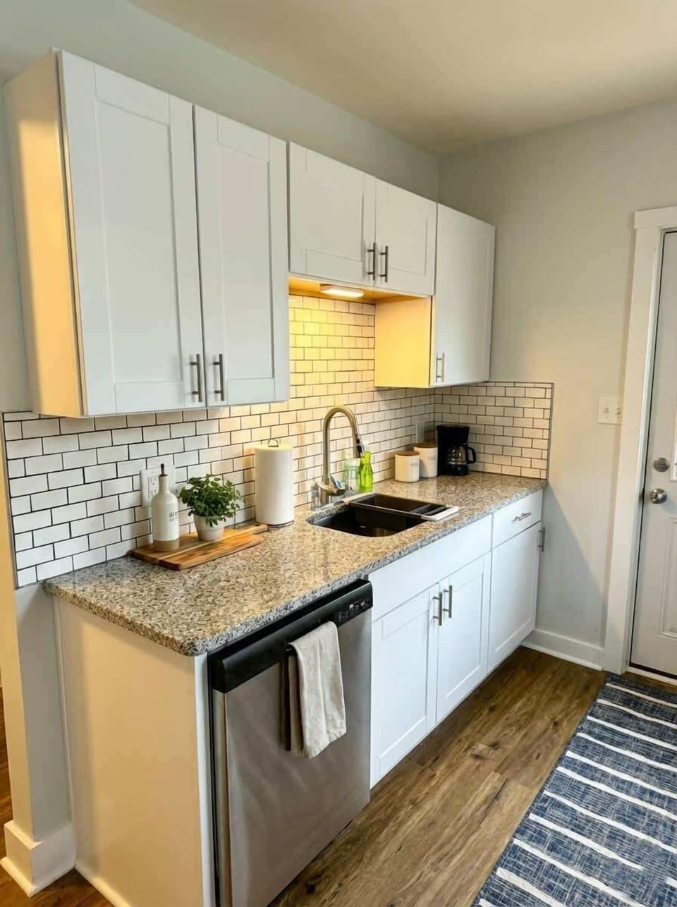 Kitchen sink area with dishwasher, white cabinetry, and subway tile backsplash.