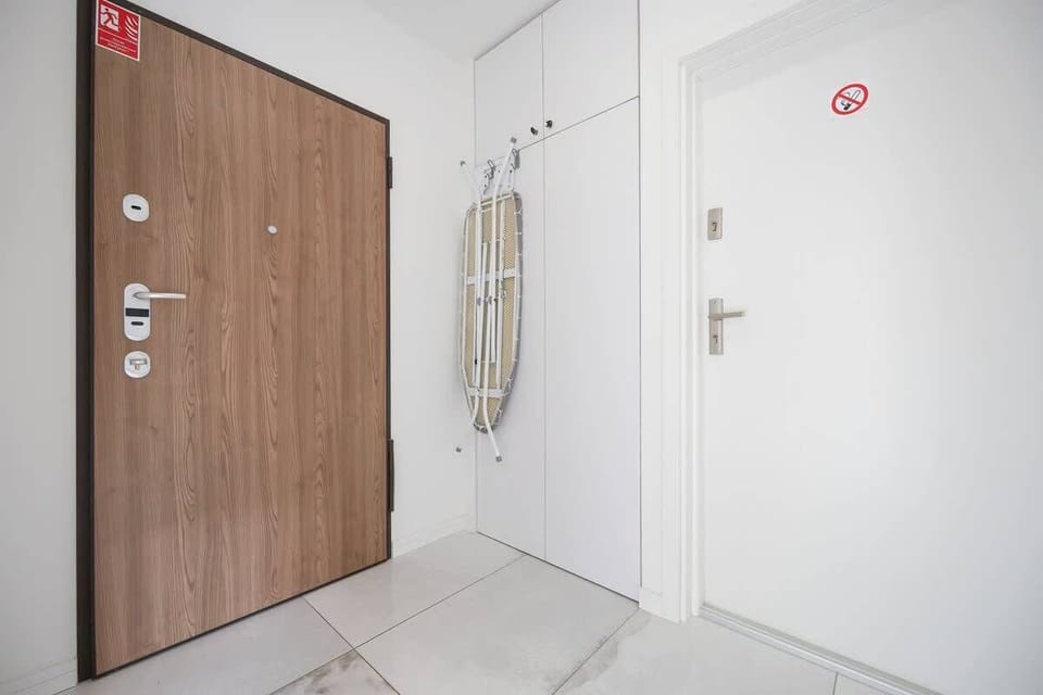 The apartment entrance featuring a wooden door, white walls, and a fire safety sign.

