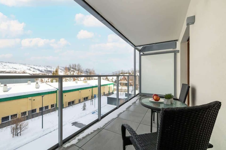 A spacious balcony with glass railings, offering a snowy mountain view and an outdoor seating area.

