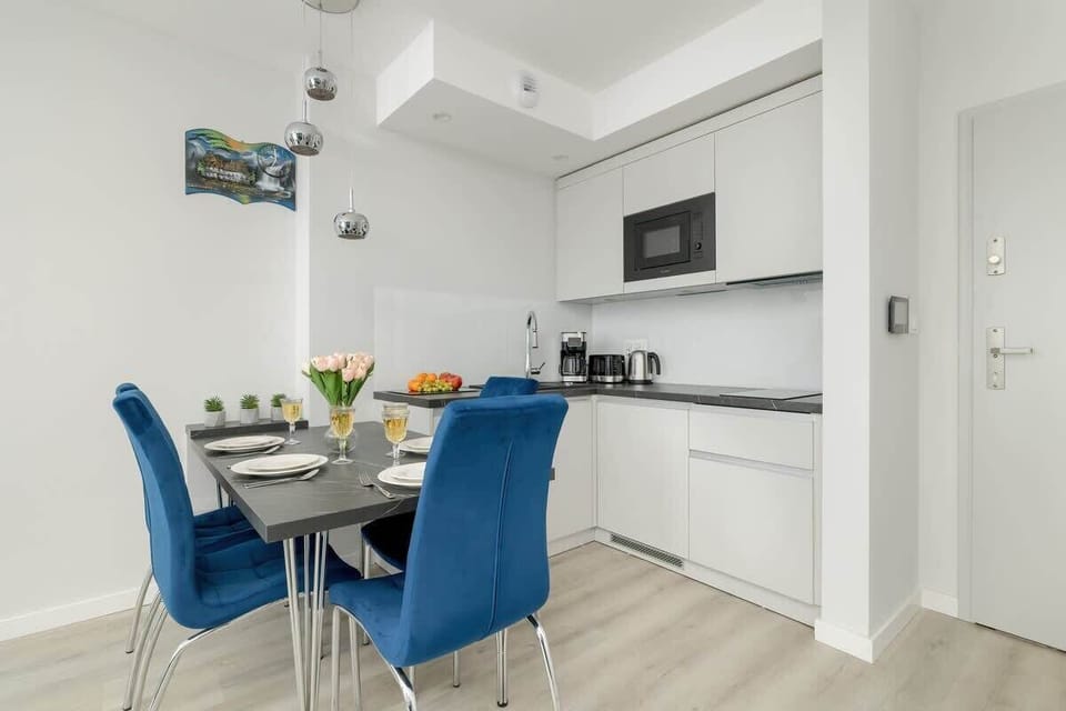 A modern dining space with a sleek white table, four blue chairs, and decorative accents.
