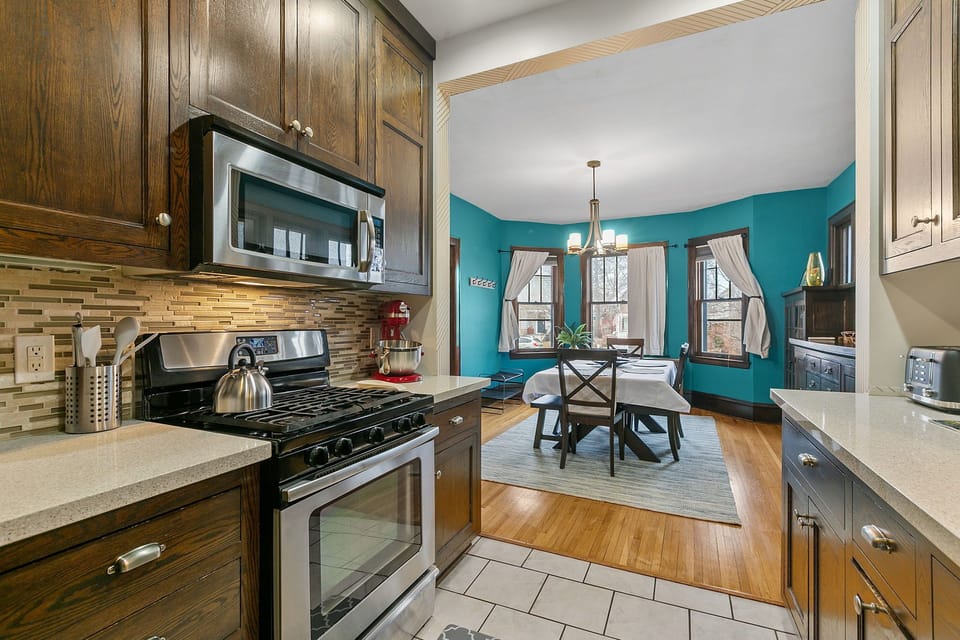 Your fully equipped kitchen features modern appliances and rich wood cabinets, flowing into a bright dining space with turquoise accent walls.