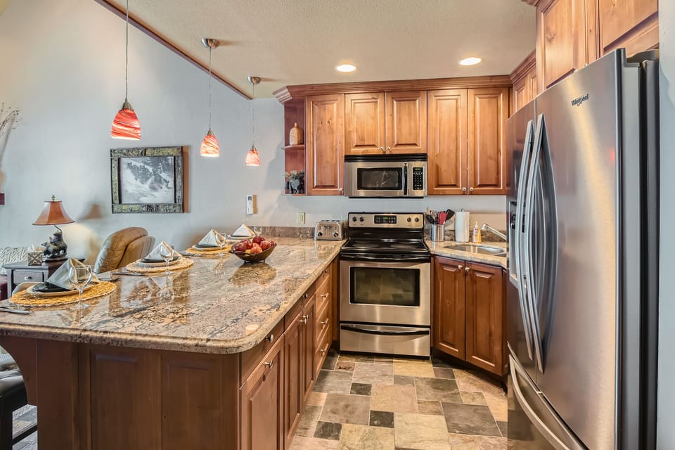Bright, fully equipped kitchen with stainless-steel appliances, granite countertops, and warm wood cabinetry. Perfect for preparing meals and gathering at the breakfast bar. A cozy, functional space designed for comfort during your Park City stay.
