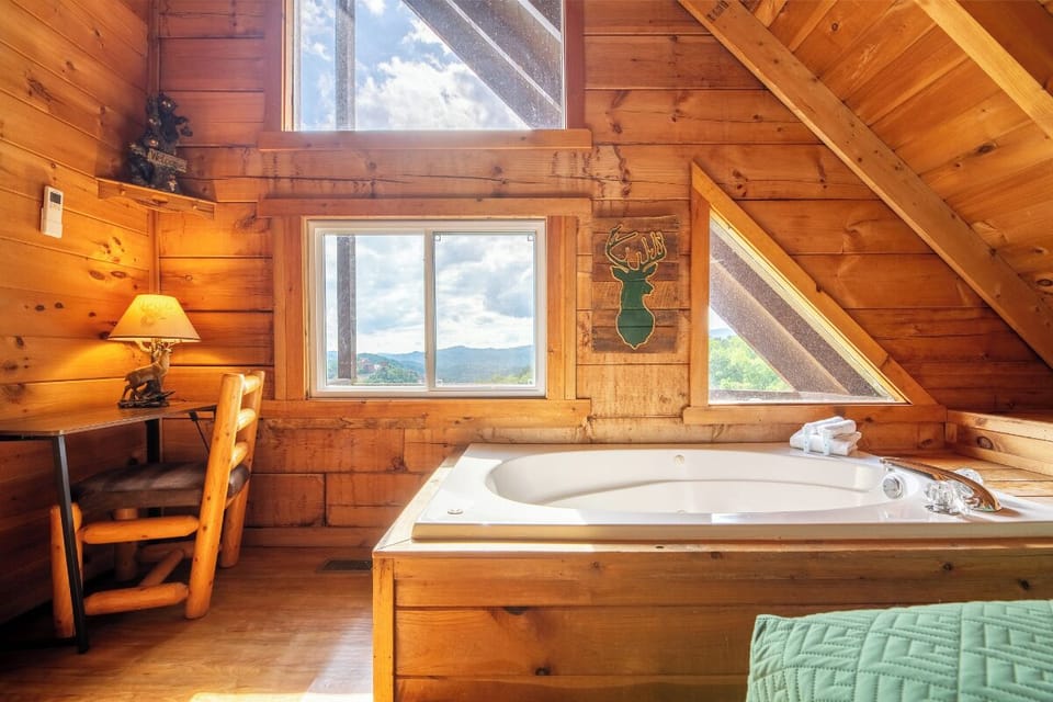 Soak in your private tub while gazing at mountain views through panoramic windows in this cozy loft retreat with warm wood beams and rustic charm.