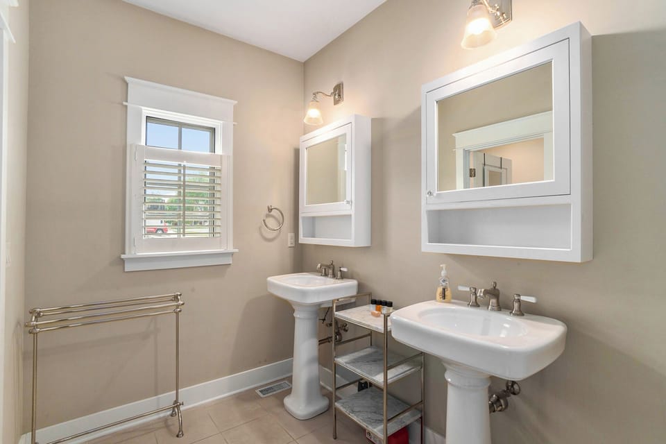 Two pedestal sinks beneath white-framed mirrors beside a bathroom window.