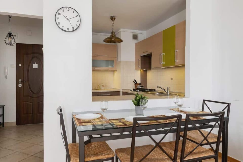A bright and spacious dining area connected to the kitchen, with a modern table set for meals, positioned under a wall clock.

