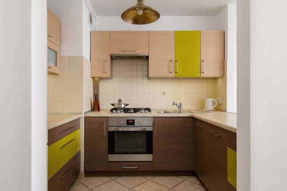 A functional kitchen with a mix of wooden and green cabinets, a built-in oven, and stylish lighting, offering a practical cooking area.

