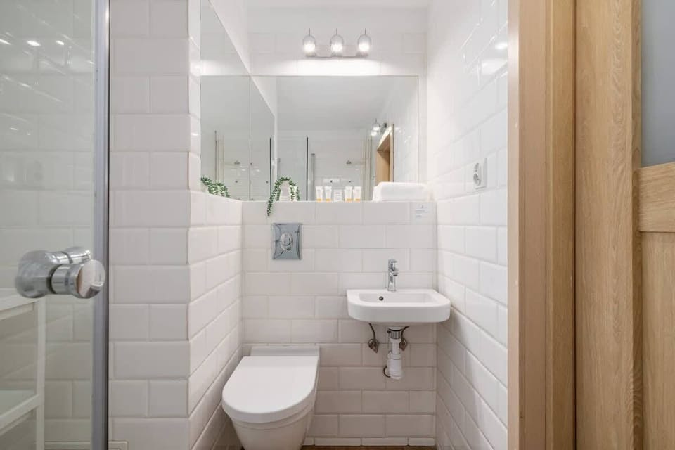A compact yet stylish bathroom with a wall-mounted toilet, a small sink, and a well-lit mirror, enhancing the bright and airy feel.
