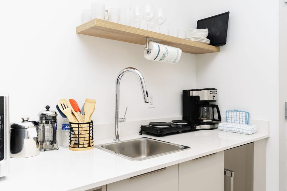 Full sink, cups, plates, wine glasses, mugs, electric stove, french press, and mini fridge
