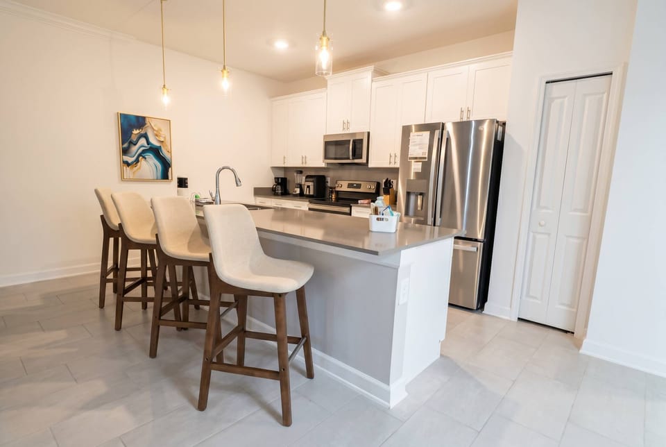 Welcome to this modern kitchen with stainless steel appliances and a chic gray island perfect for casual dining. The warm wood accents of the bar stools and soft lighting create a cozy space for meal prep or relaxed chats.