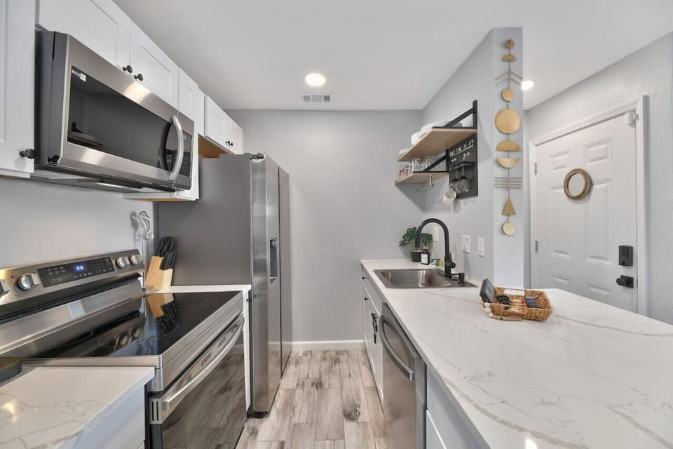 Modern kitchen with stainless appliances, cookware, dishes, and utensils