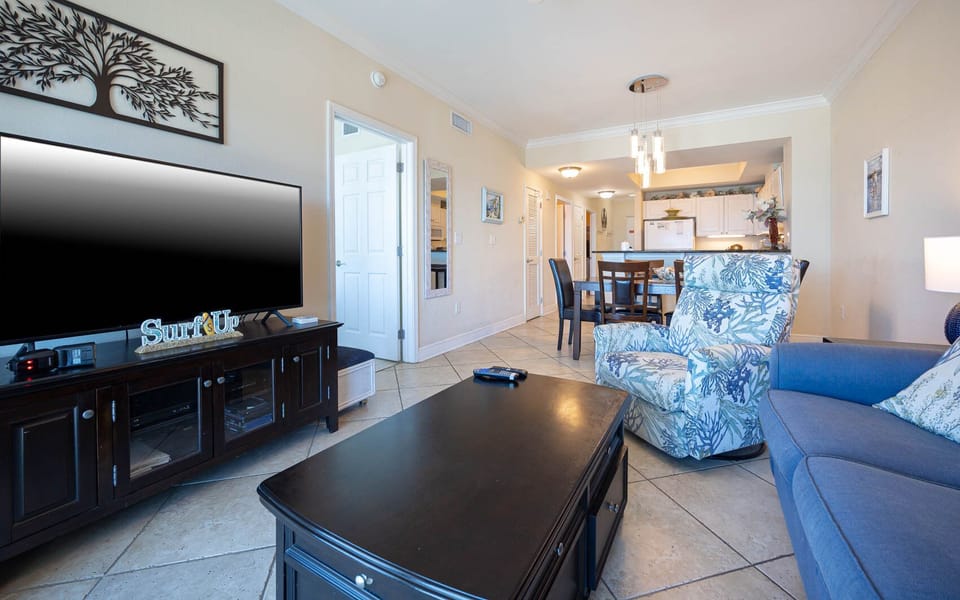 This inviting living area features a large TV, stylish seating, and a view of the bright, open kitchen
