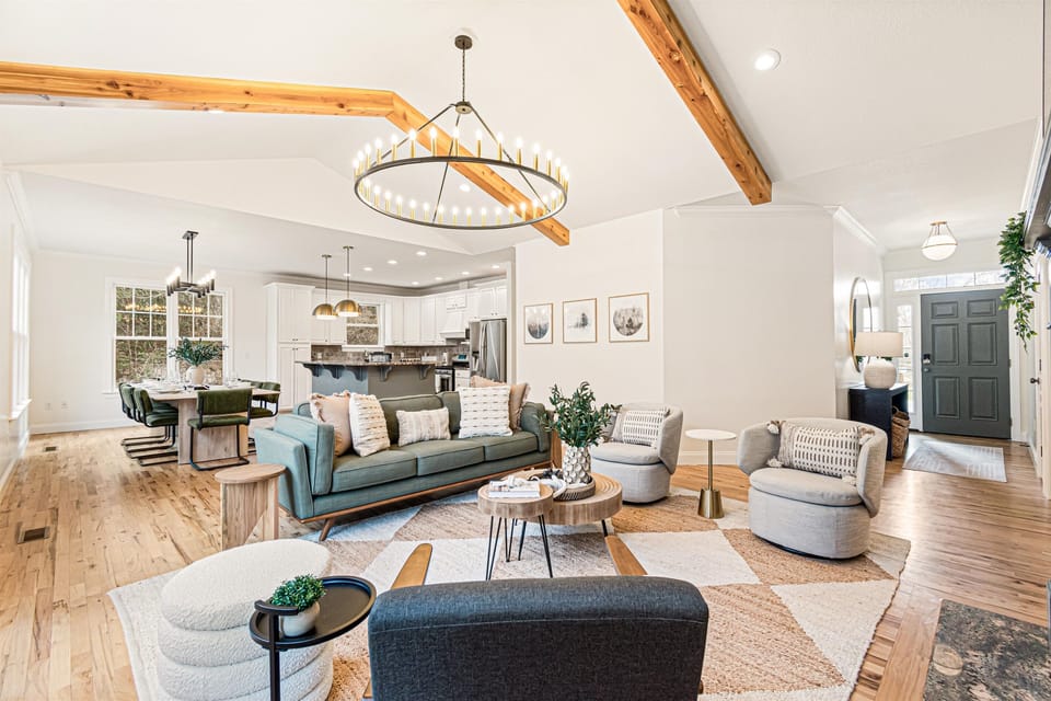 Open floor plan connecting the living room, dining area, and kitchen — exposed beams, a statement chandelier, and hardwood floors throughout the main level.