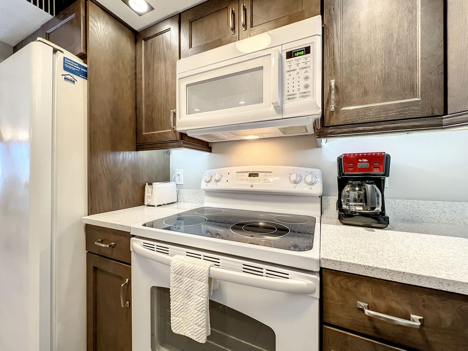 A modern kitchen with sleek appliances, featuring a microwave, electric stove, and coffee maker, offering everything needed for convenient and cozy meal preparation.