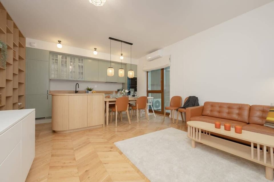 A wider view of the open-plan living area, showcasing the kitchen, dining space, and a cozy sitting area with wooden and pastel-toned accents.

