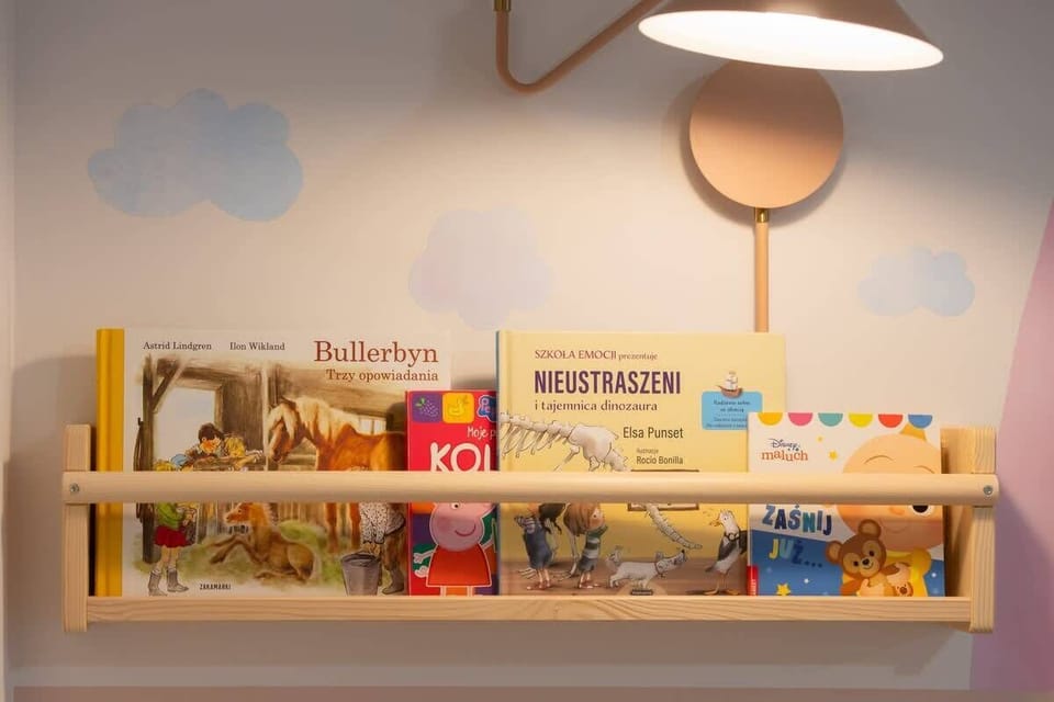 A close-up of a children's reading nook with a wall-mounted wooden bookshelf, soft lighting, and a charming cloud-shaped decoration.

