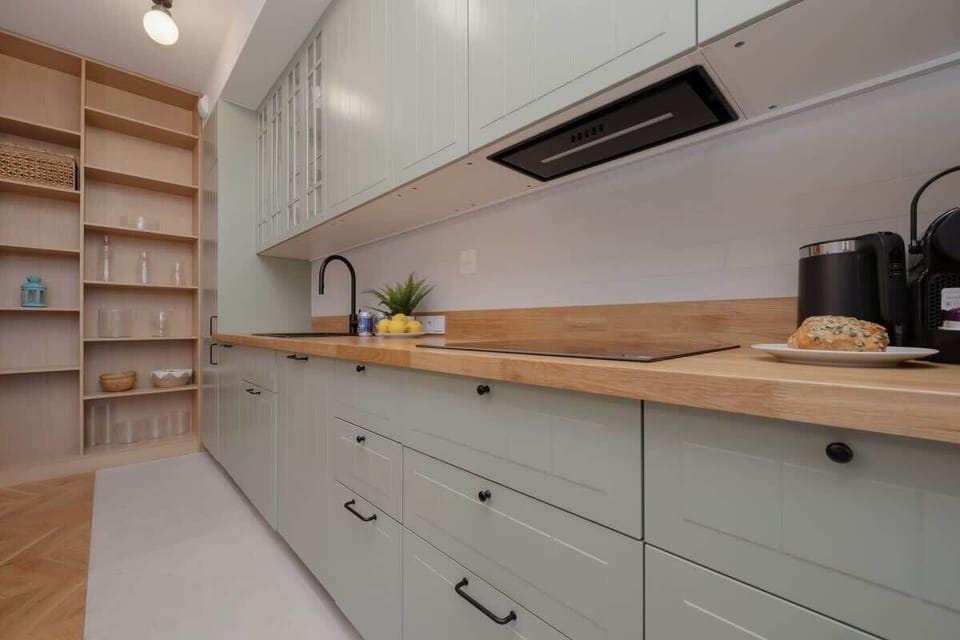A sleek kitchen with light green cabinets, wooden countertops, and open shelving, creating a modern and well-organized cooking space.

