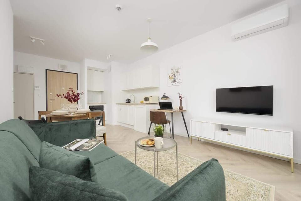 Another angle of the living room, highlighting a sleek wall-mounted TV, a wooden media unit, and an airy, well-lit space.

