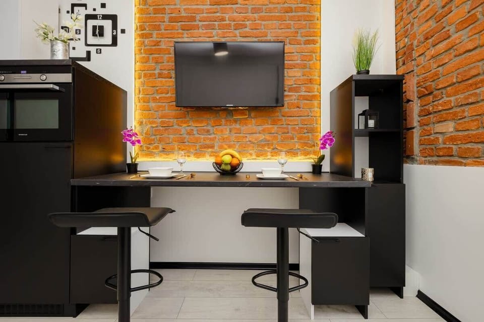 A cozy dining and entertainment area with a wall-mounted TV, a stylish black dining set, and a warm brick feature wall for a contemporary look.


