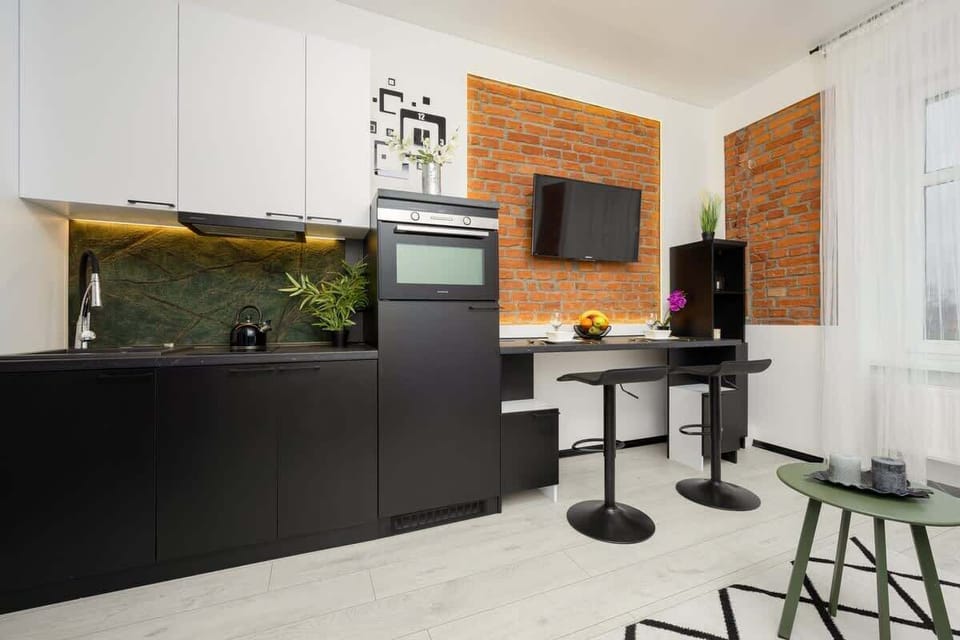 Another angle of the kitchen and living area, showing the cohesive black and white color scheme with warm brick tones for contrast.

