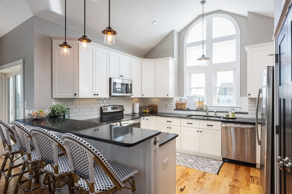Modern Coastal Kitchen w/ Stainless Steel Refrigerator, Electric Range, Microwave, Sink, Dishwasher, Cooking Utensils, and Kitchen Bar Chairs