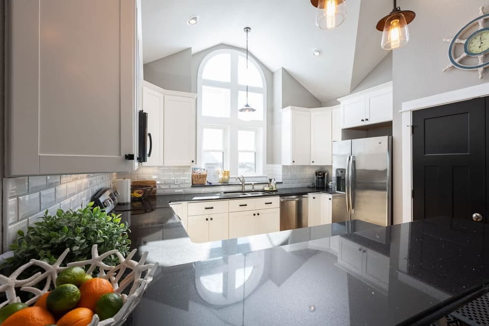 Modern Coastal Kitchen w/ Stainless Steel Refrigerator, Electric Range, Microwave, Sink, Dishwasher, Cooking Utensils, and Kitchen Bar Chairs