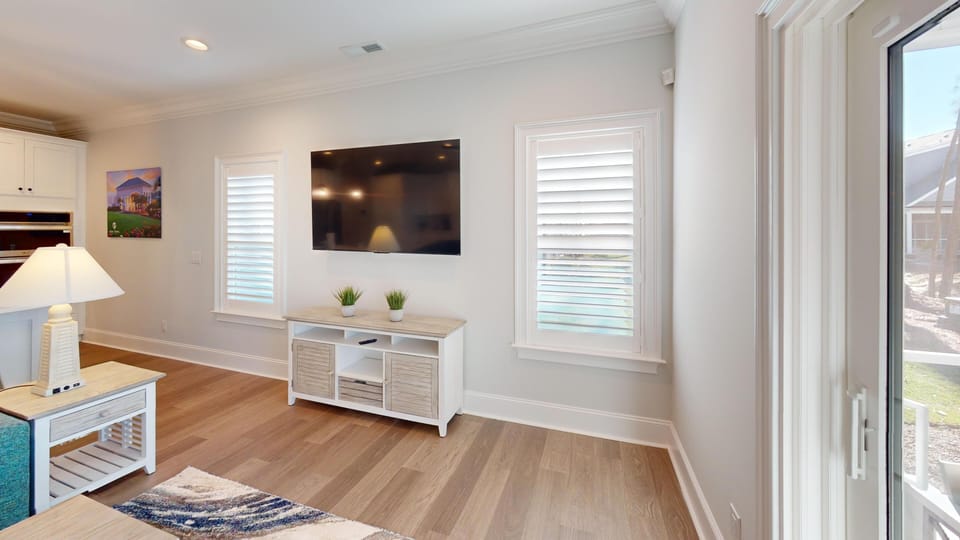 Open-plan living room with comfortable seating, big-screen TV, and natural light streaming through large windows.