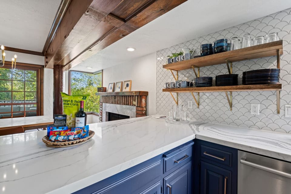 Bright kitchen corner w/ open shelving, white tile backsplash & wide windows.