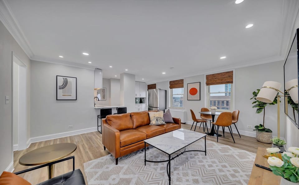 Bright open living area w/ leather sofa, patterned rug & seamless flow into dining & kitchen