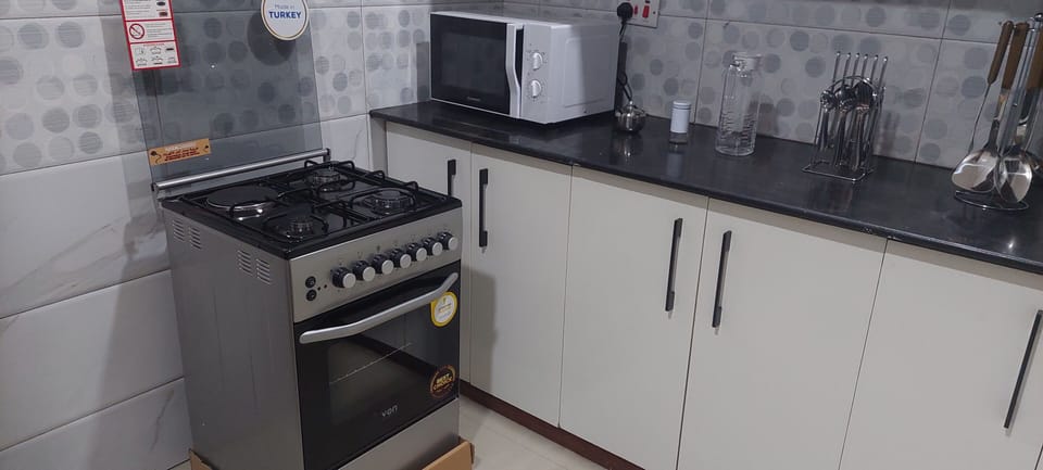 Full kitchen with cooker, microwave, refrigerator, kettle, dining ware & pots.