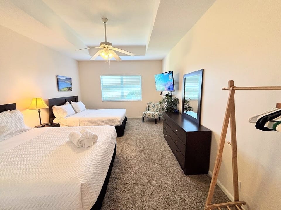 Spacious bedroom featuring two comfortable beds, TV, ceiling fan, dresser storage, and a convenient luggage rack.