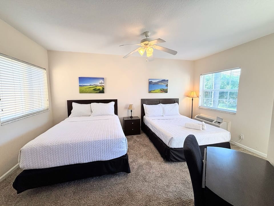 Comfortable bedroom featuring two beds, ceiling fan, dresser storage, and plenty of natural light.