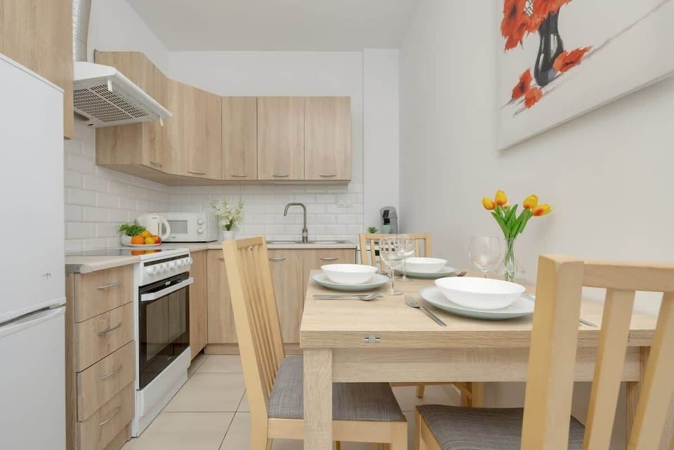 Another view of the dining space, showcasing a wooden table with matching chairs, warm lighting, and a practical kitchen layout.

