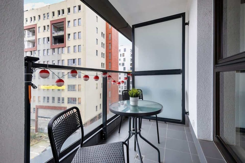 A private balcony with a small table and chairs, decorated with potted plants, providing a relaxing outdoor space with a view of the city.

