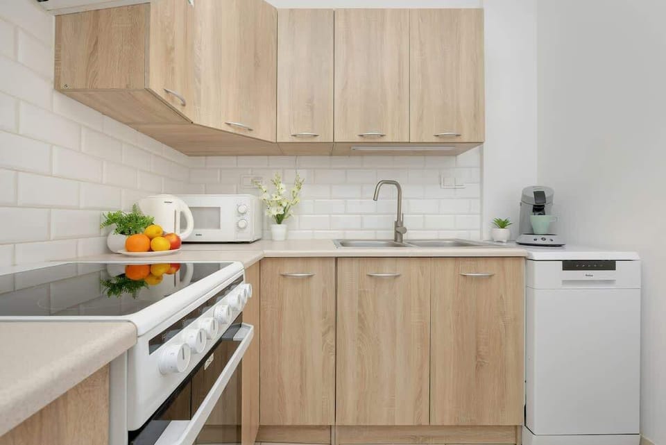 A different perspective of the kitchen, emphasizing the wooden cabinetry, white countertops, and modern appliances.

