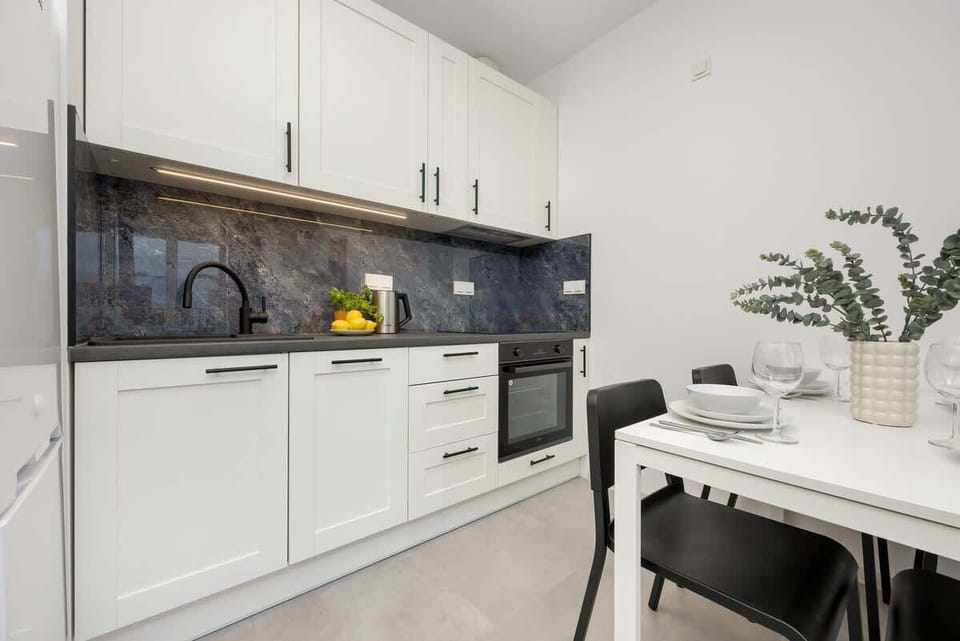A close-up of the kitchen workspace, highlighting the modern white cabinets, black countertops, a stylish backsplash, and a decorative plant.

