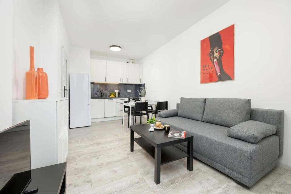 A different angle of the living room, focusing on the gray sofa, a black coffee table, and the white cabinet with bright orange vases and a red painting.

