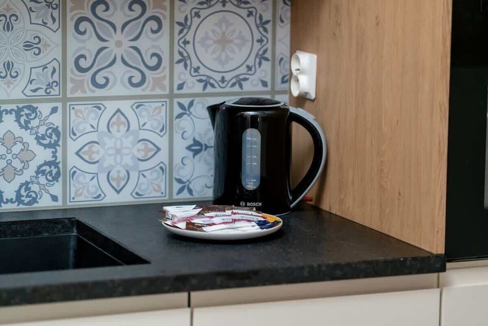 A close-up of the kitchen counter with a black kettle, decorative backsplash tiles, and a neatly arranged countertop.

