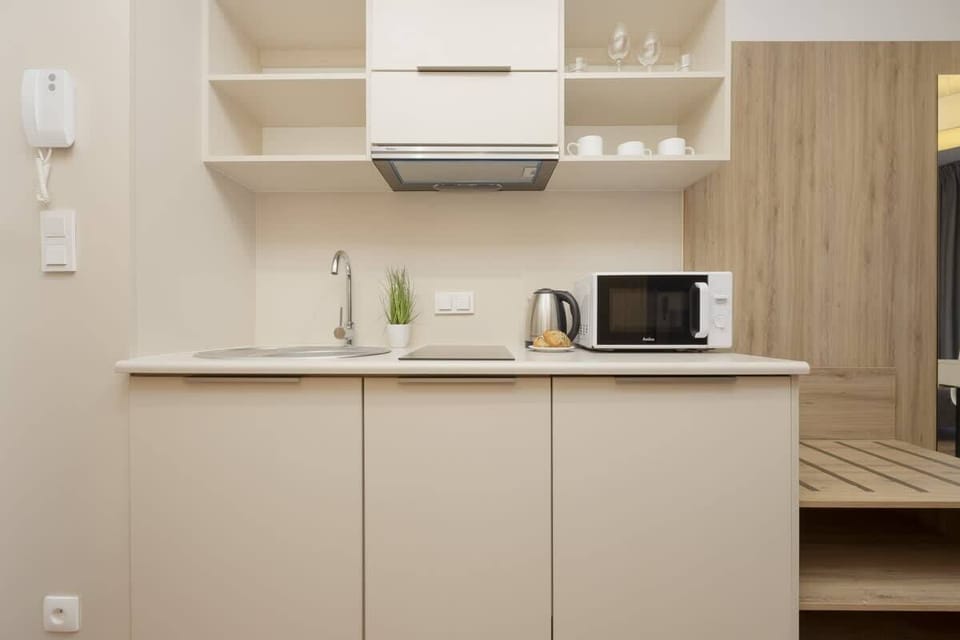 A compact kitchenette with modern white cabinetry, equipped with a microwave, kettle, and storage shelves for convenience.

