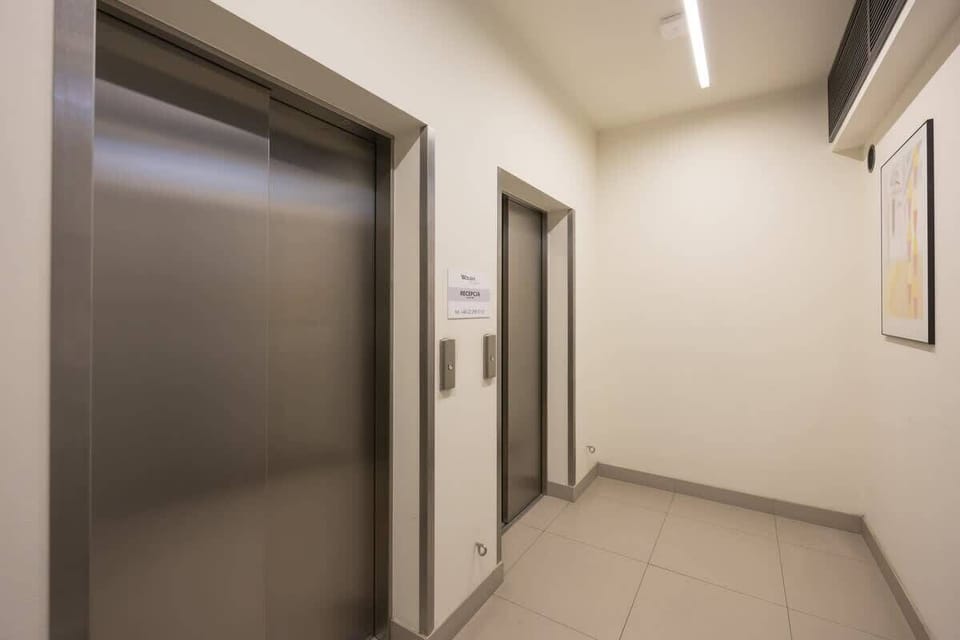 A hallway leading to an elevator, with beige walls and modern lighting, ensuring easy accessibility within the building.

