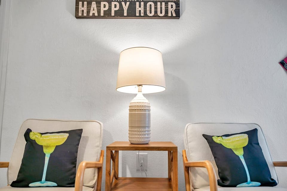 Cozy reading nook w/ an accent chair, warm lamp light, and colorful pillows to unwind.