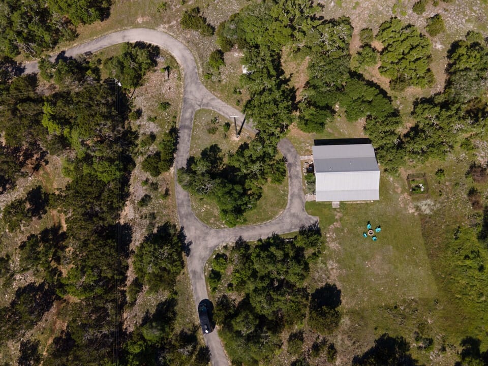 Nestled on 100 acres in Wimberley, this idyllic country cottage boasts rustic charm with modern comforts. Surrounded by rolling hills and mature trees, it features a cozy porch, open living spaces with wooden beams, a stone fireplace, and breathtaking views.