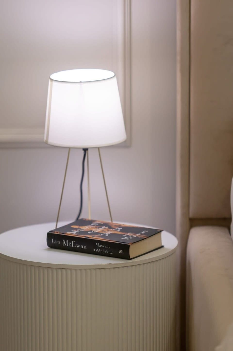 A close-up of a modern bedside table with a sleek white lamp, offering soft ambient lighting.

